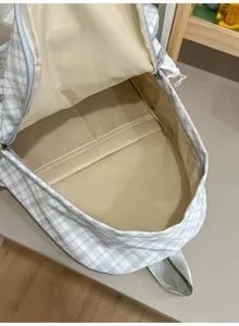 Gros plan sur la doublure beige, l’ouverture zippée et le tissu à carreaux bleu et blanc du sac.