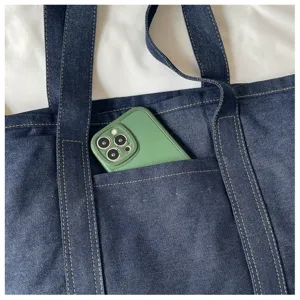 Vue détaillée de la poche avant du sac cabas en denim bleu foncé avec des coutures solides.