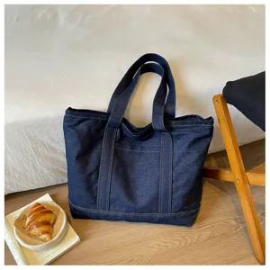 Grand sac cabas en denim bleu avec doubles anses et poche avant pour usage quotidien.