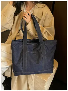 Vue détaillée du sac cabas en denim bleu foncé, avec des lanières robustes et une poche avant.