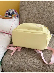 Detailed view of a light yellow women's backpack with pink straps and cute front embroidery.