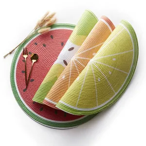 Gros plan de sets de table tressés colorés en forme de fruits avec couverts et herbe.