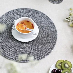 Détail du set de table tressé rond avec motif tissé texturé gris dans un décor de table.