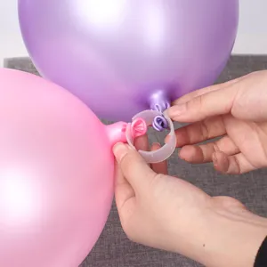 Detail shot showing hands using white plastic balloon clips to assemble arch balloons securely.