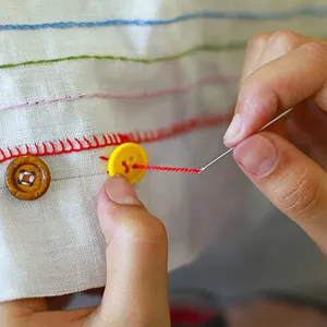 Dettaglio ago da cucire a mano con ricamo e applicazione bottoni su tessuto bianco