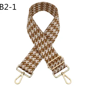 Detailed view of brown and white houndstooth jacquard bag strap with gold adjustable metal hardware.