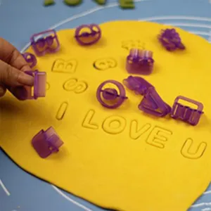 Detail view of purple plastic alphabet cookie cutters pressing text on yellow dough for baking.