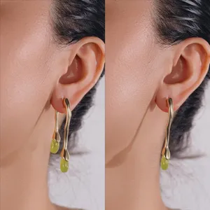 Détail en gros plan de boucles d'oreilles pendantes dorées organiques avec pierres vertes.