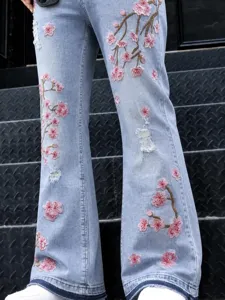 Jean droit bleu clair pour homme avec broderie de fleurs de prunier roses et détails usés.