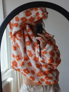Zachte witte fleecetrui met opvallende oranje bloemenprint en handige halve ritssluiting.