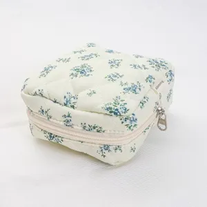 Close-up detail of quilted floral cosmetic pouch with zipper and side fabric brand tag.