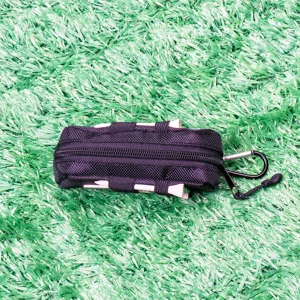 Close-up detail of black golf ball storage pouch with tees and carabiner on green turf.