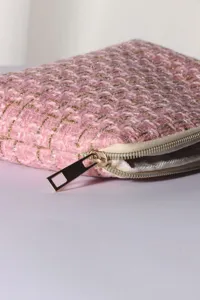 Close-up of a stylish pink tweed cosmetic pouch featuring a textured fabric and a gold zipper.