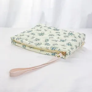 Quilted cosmetic bag detail featuring blue floral print, pink wrist strap, and zipper.
