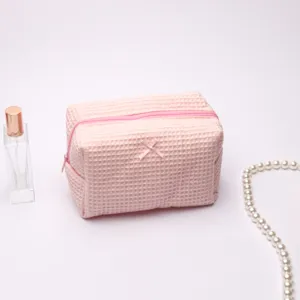 Pink waffle cosmetic bag detail showing soft fabric texture, smooth zipper, and cute bow accent.