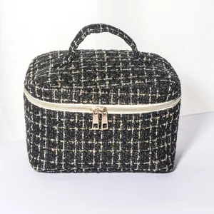 Black gold tweed cosmetic bag with top handle and double zipper for portable travel storage.