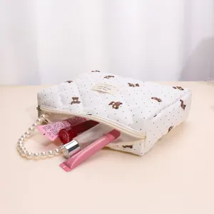 Quilted cosmetic bag with cute bear pattern, pearl handle, and spacious storage for travel use.