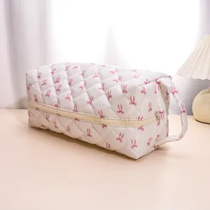 Detailed view of white quilted cosmetic travel bag with pink bow pattern and zipper closure.