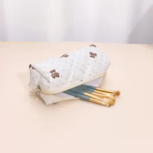 Detail view of white quilted cosmetic bag featuring cute bear pattern and makeup brushes.