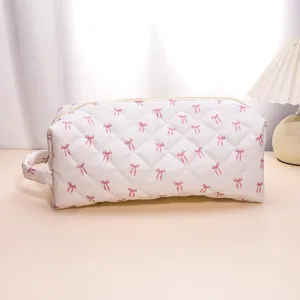 Close-up of the quilted white cosmetic bag with pink bows, showing texture and portable handle detail.