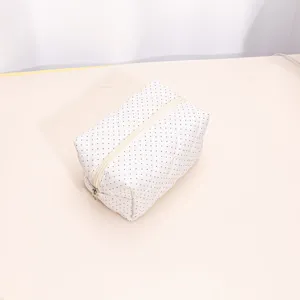 Detailed view of white quilted cosmetic bag with black polka dots, soft texture and smooth zipper.