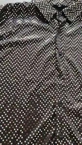Primo piano dei dettagli della camicia nera con pois di paillettes lucide e bottoni.