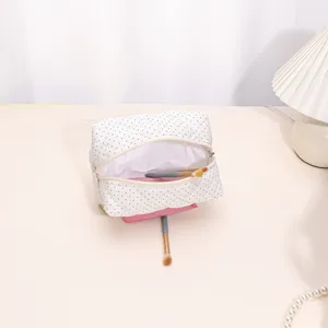 White quilted cosmetic bag with black polka dots, open view showing makeup brushes inside.