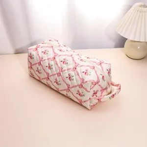 Close-up detail of quilted floral cosmetic bag featuring pink ribbon and rose pattern.