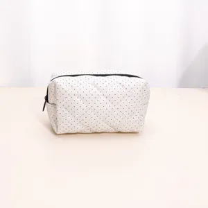 Detailed view of white quilted makeup bag featuring black polka dots and secure zipper.