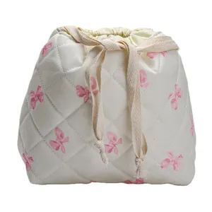 Detailed view of quilted drawstring cosmetic bag, soft beige fabric with pink bow print.