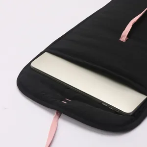 Black quilted laptop sleeve detail view with pink ribbon tie and silver laptop inside.