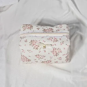 Floral quilted cosmetic bag with lace trim and bow pendant, portable zipper toiletry pouch for women.