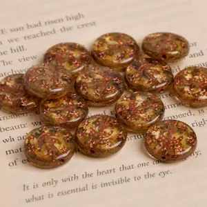 Close-up detail of amber glass coin beads with copper star and moon patterns on a book page.