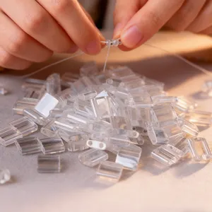 Close-up shot of hands crafting with clear square two-hole beads, DIY jewelry making process.