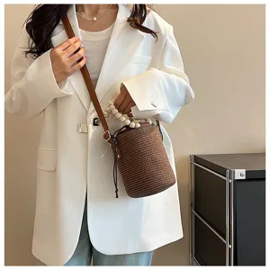 Chic woven straw bucket bag with pearl handle and shoulder strap for summer beach vacation.