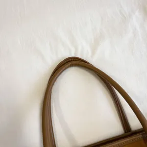 Detalle en primer plano del asa del bolso de cuero marrón, acabado premium y costuras.
