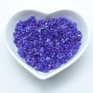 Purple glass triangle seed beads packed in a white heart bowl for jewelry making crafts.