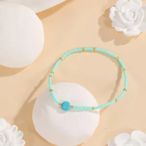 Turquoise blue seed bead bracelet detail view with gold spacers and central stone on art prop.