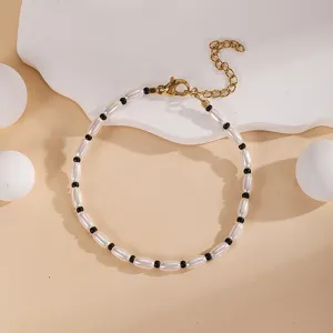 Detail shot of white rice bead and black round bead layered bracelet with gold extension chain.