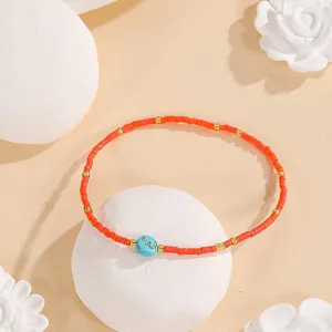 Detailed view of handmade beaded bracelet with red seed beads, gold spacers and turquoise.