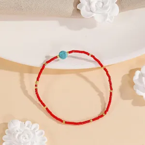 Close-up detail of the red seed bead bracelet with turquoise center stone and gold spacer accents.