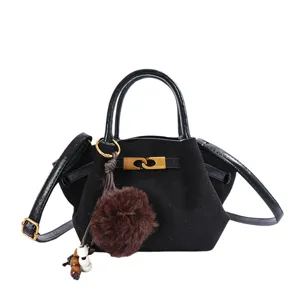 Black suede mini handbag with top handle, gold metal clasp and fluffy pom-pom pendant.