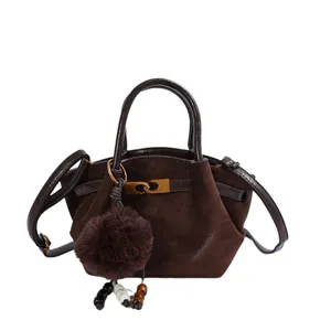Vintage brown suede shoulder bag with stylish metal clasp and cute plush pom-pom charm.