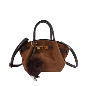 Detailed view of brown suede shoulder bag with top handle and cute plush ball pendant.