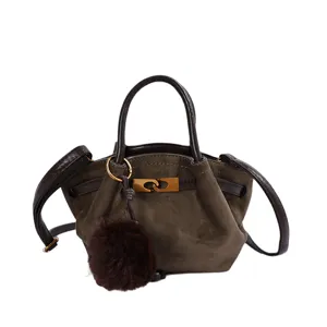 Close-up of vintage suede handbag showing fine texture, metal lock, and fluffy pom-pom charm.