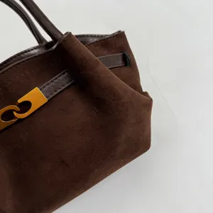 Close-up detail of the retro brown suede handbag showing texture, strap, and gold metal clasp.