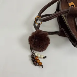 Detailed view of the dark brown suede handbag featuring a cute plush pom-pom and wooden bead charm.