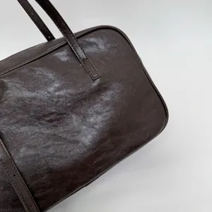 Close-up detail of dark brown leather boston bag featuring soft crumpled texture and slim strap.
