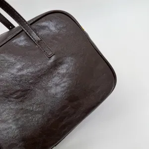 Close-up detail of retro brown crinkled leather handbag showing fine texture and stitching.