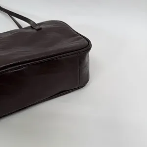Close-up detail of dark brown leather shoulder bag, textured surface, minimalist commuter style.